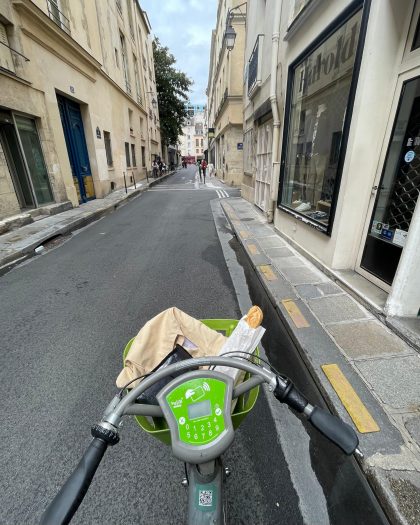 Riding a Vélib' bike on a street in Paris, with a baguette in the basket