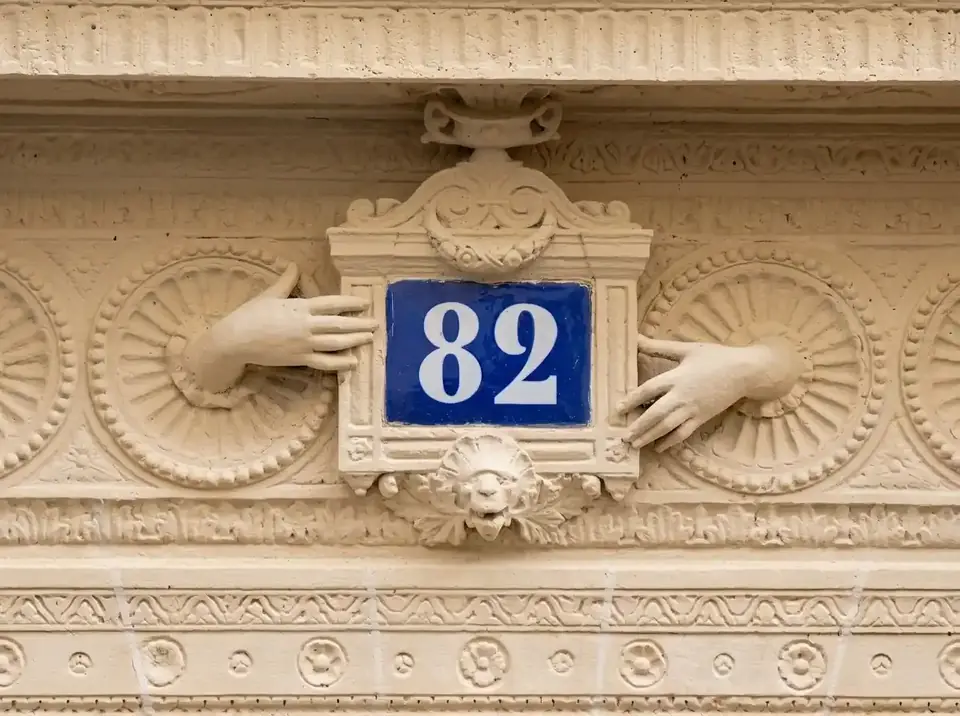 שתי ידיים מפוסלות אוחזות במספר הבית ב-82 rue Blanche